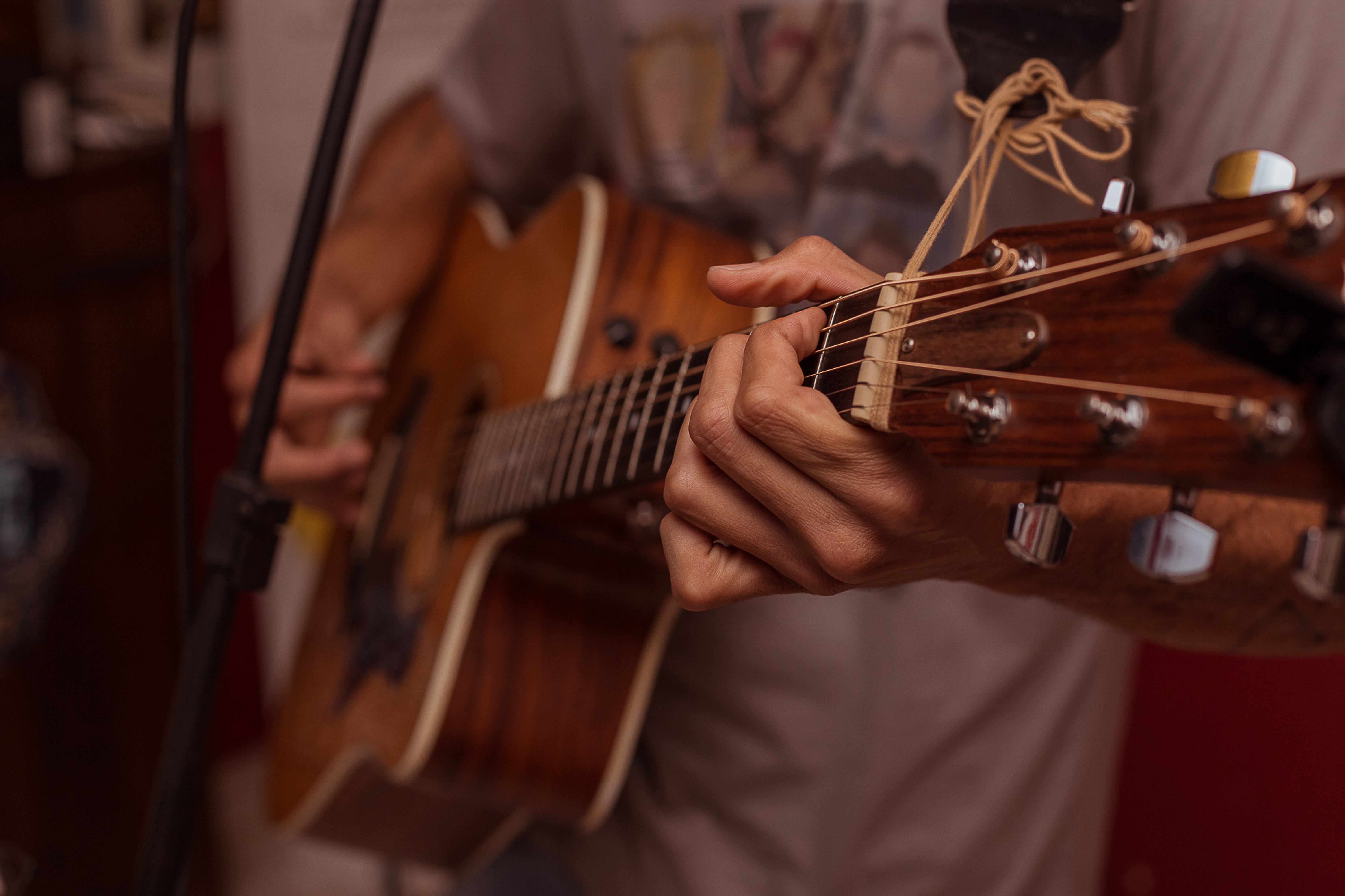 man learn to play guitar, acoustic guitar, down strumming in low light, with mic stand in foreground 