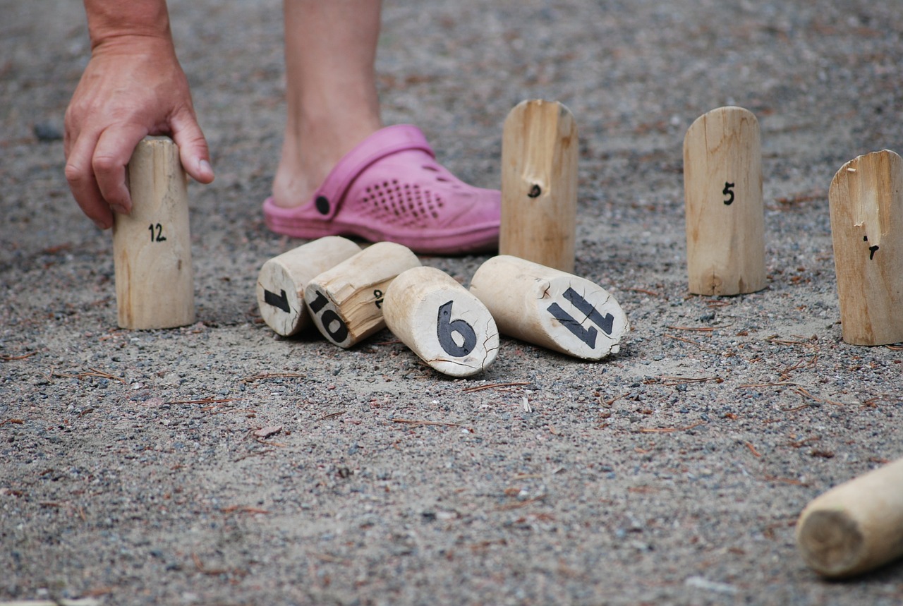pink croc and persons hand, person is bending over to pick up wooden dowels with various numbers written on them