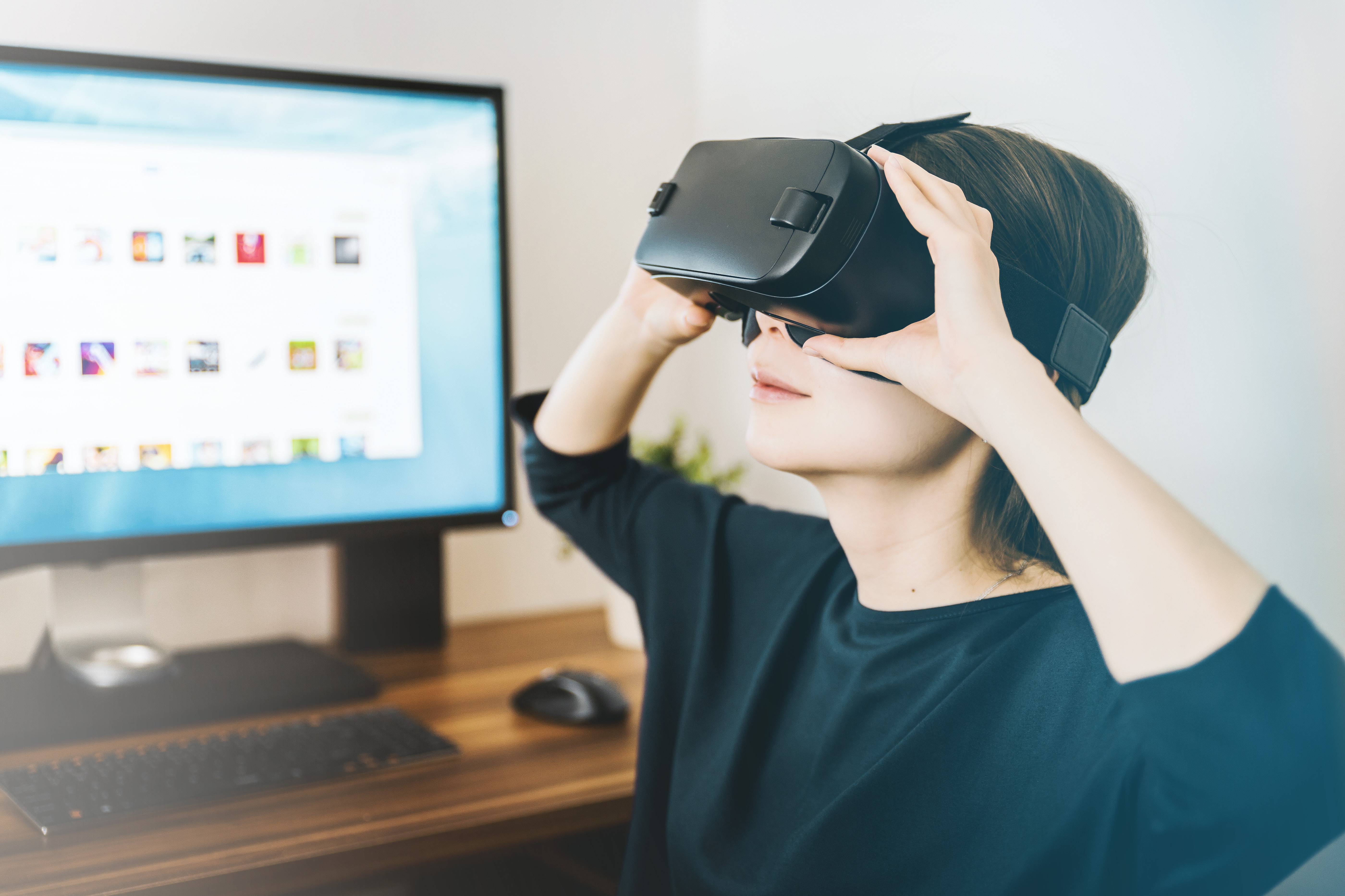 woman sitting wearing Virtual Reality headset in front of computer screen