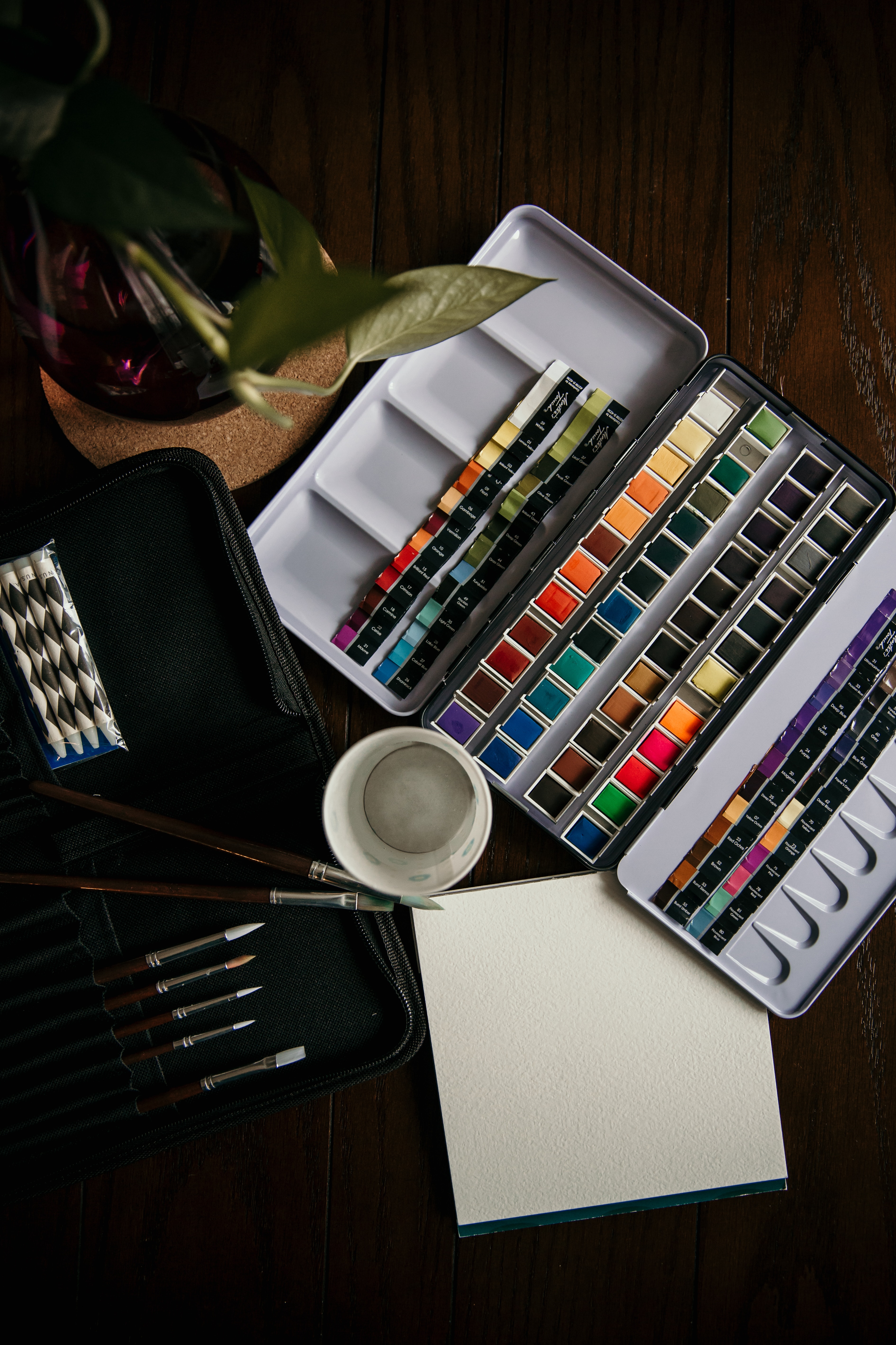 watercolor paint set set on table overview with watercolor brushes and cup of water