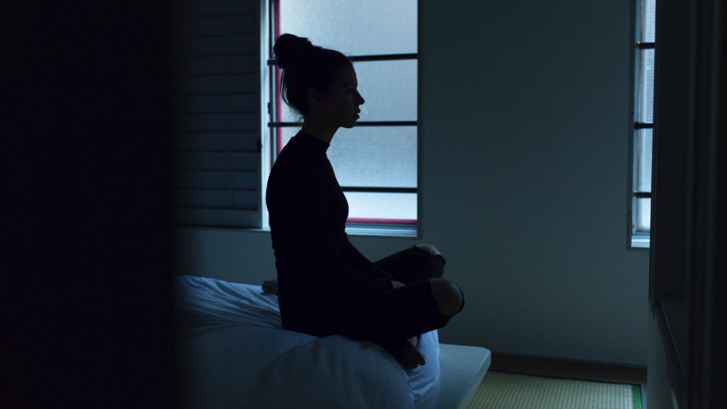 daily meditation benefits, woman sitting on edge of bed in dark room