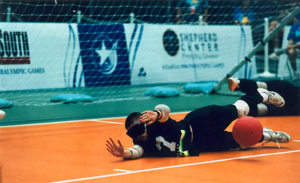adaptive sport goalball, image shows player laying out on the ground to stop goalball from entering the net behind her