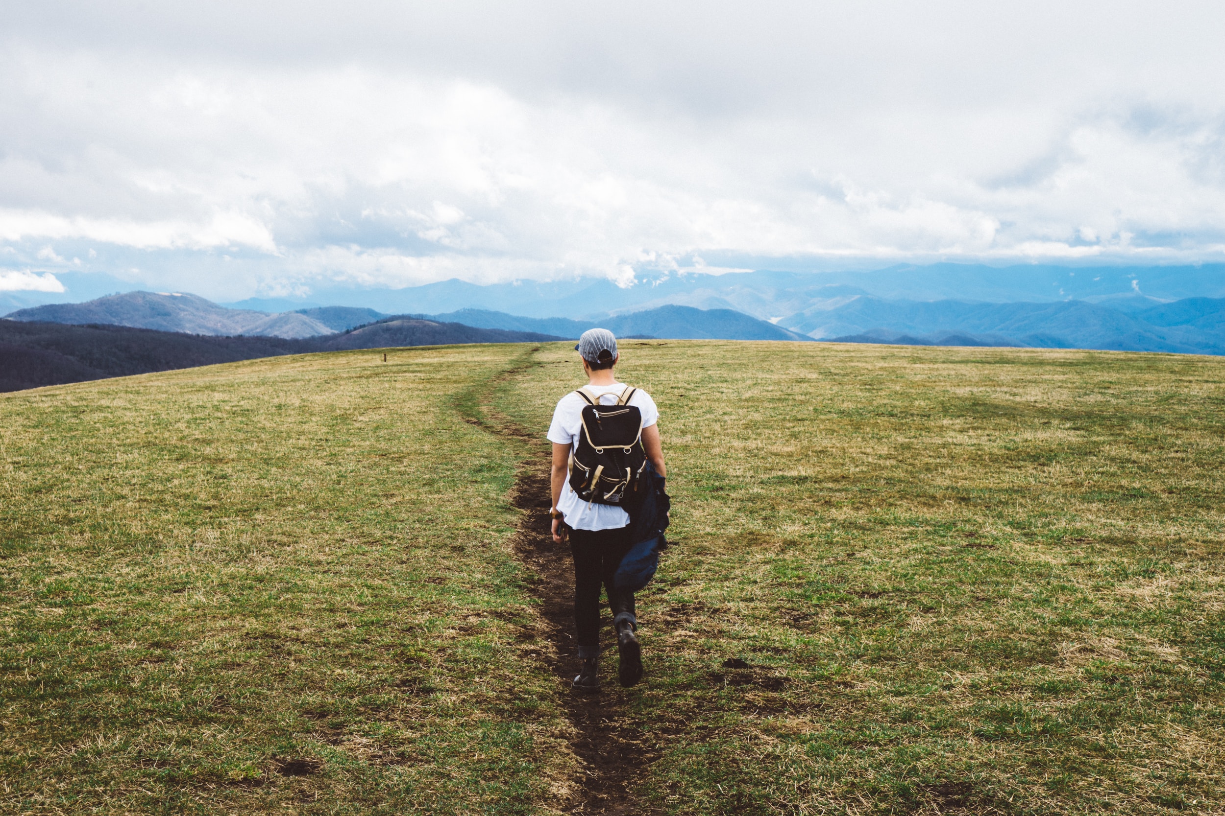man hiking on path with backpack towards mountain range