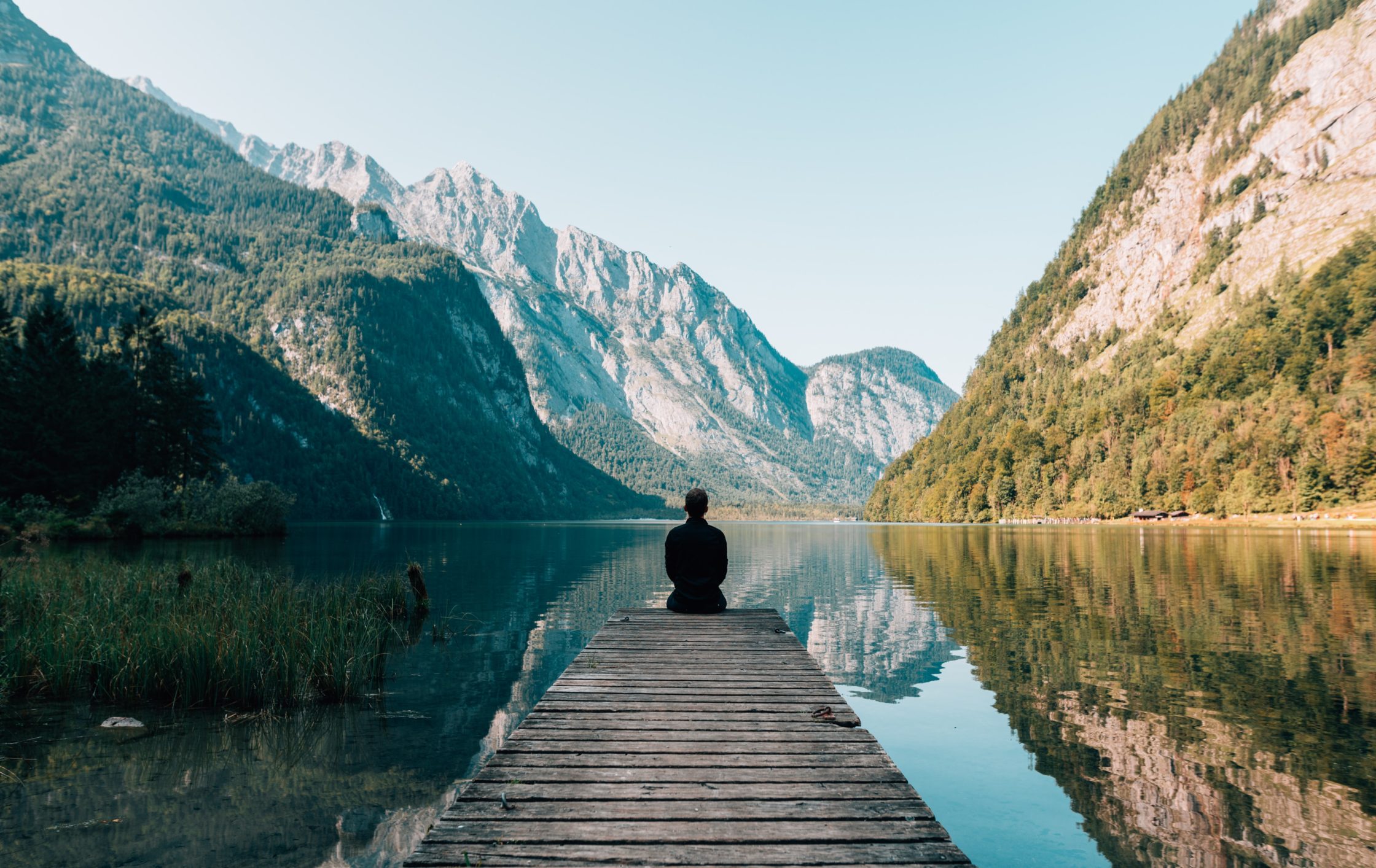 man meditating outdoors, overlooking mountain and lake scene. blue sky