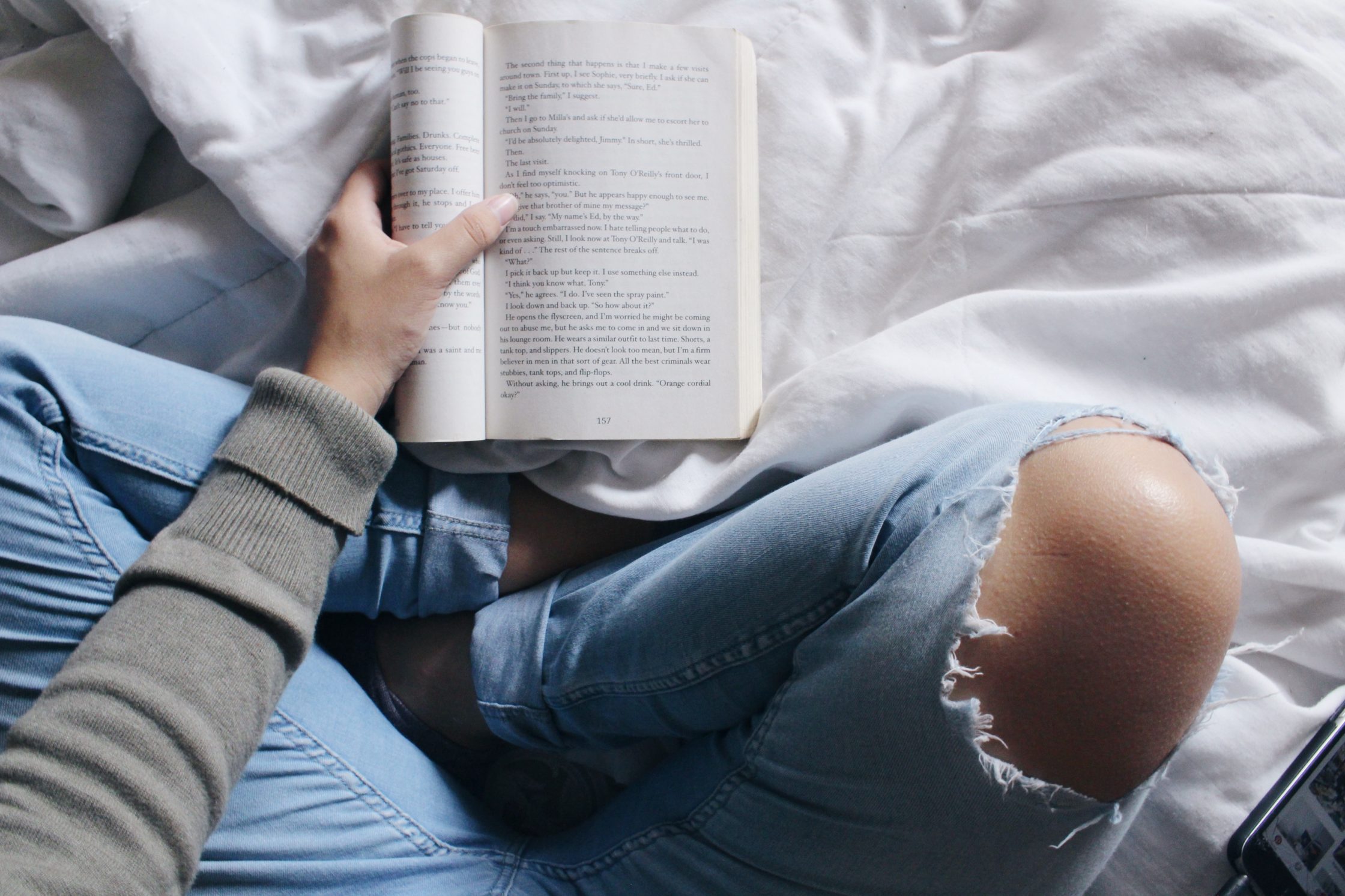 benefits of reading, woman sitting on bed reading from open book