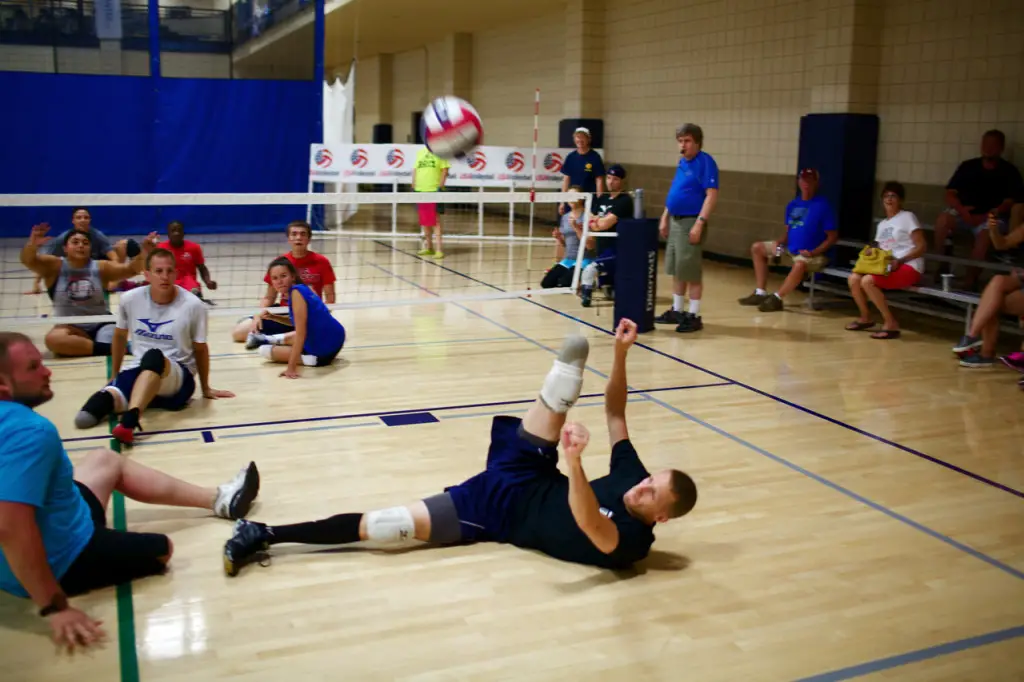 fun and popular adaptive sports include sitting volleyball, man laying out to hit volleyball up to his teammate 