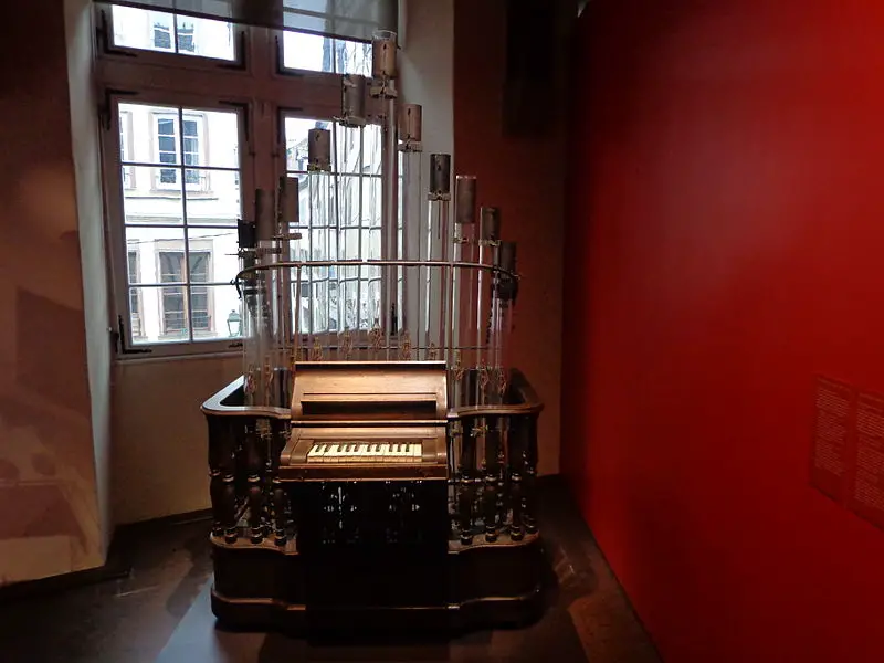 pyrophone, explosion organ in a room by a window. Next to a red wall