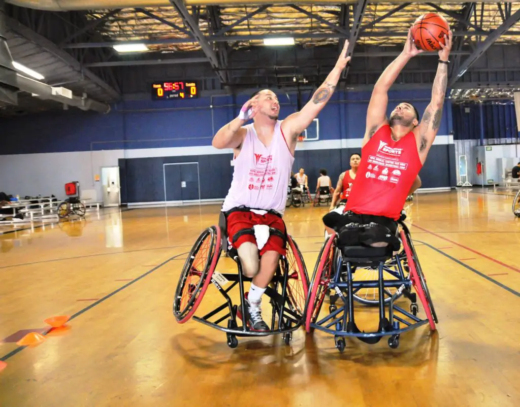 adaptive sport wheelchair basketball. Man reaching up to make a layup. Player on opposing team reaching to block him