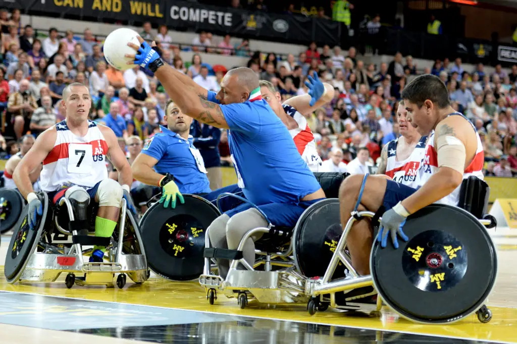 adaptive sport wheelchair rugby, action shot, man reaching ball to score point with opposing team attempting to stop him