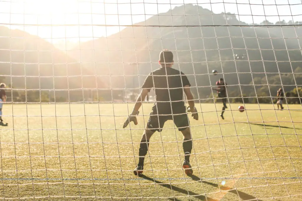 man standing in front of soccer net blocking soccer ball