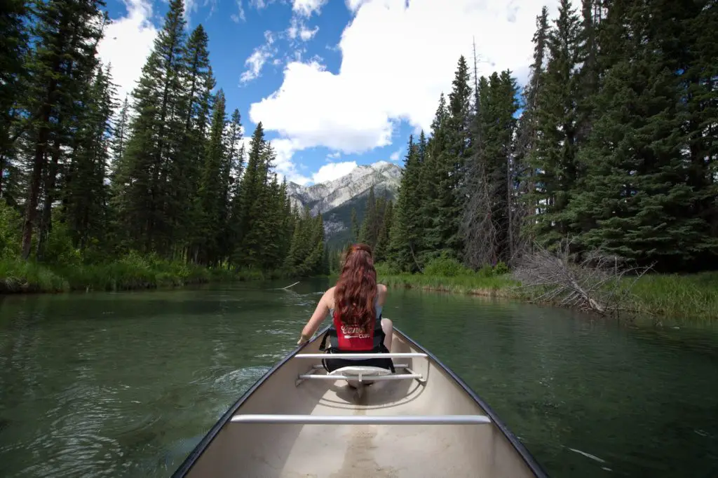 woman at the front of a canoe going down a river, mountain in the distance