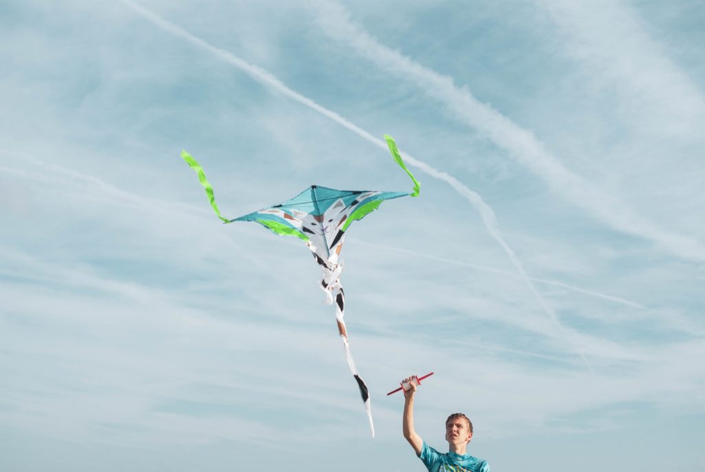 man flying a kite against blue sky; kite flying hobby