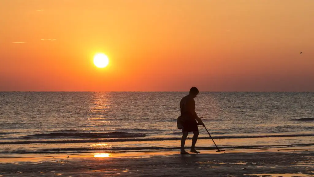 man using a metal detector on the beach at sunse
