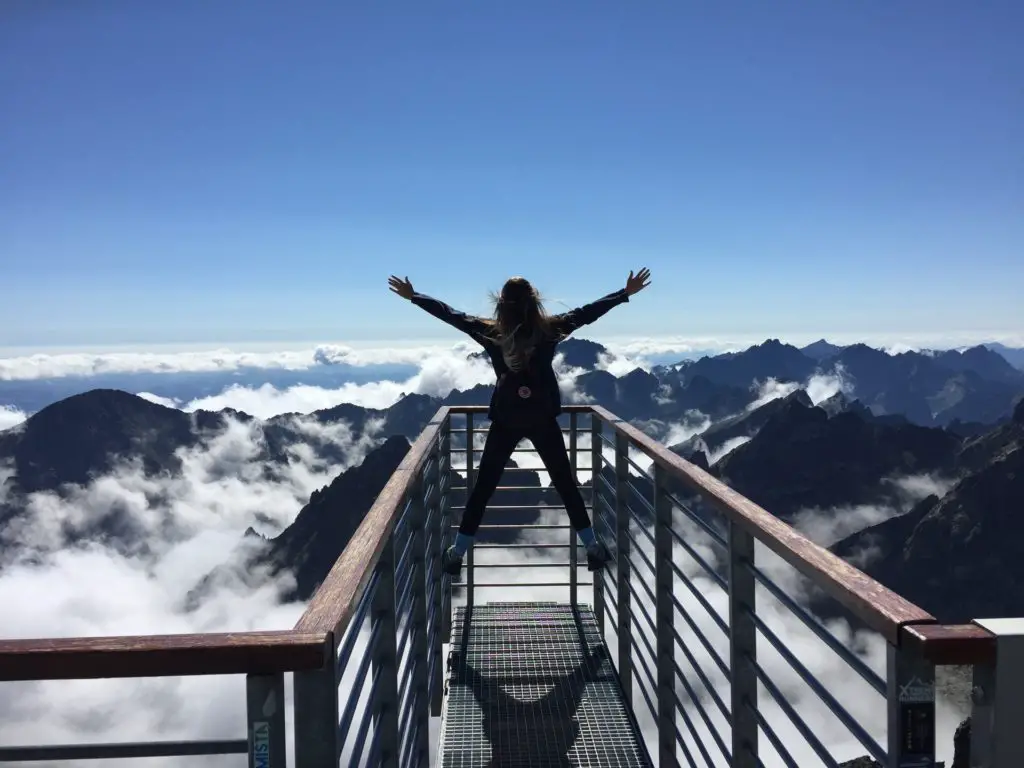 woman hiking, standing at the end of an outlook looking at mountains with her hands up