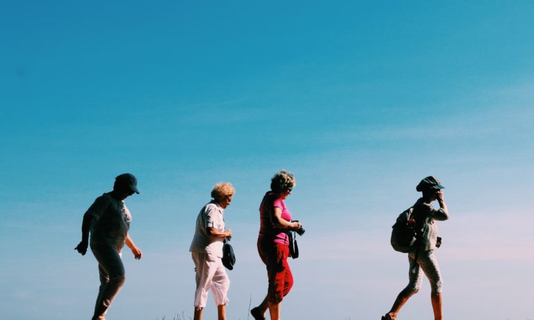 four women walking against blue sky background