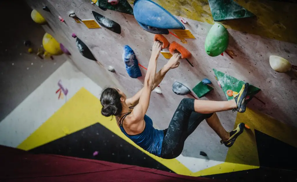 woman bouldering in climbing gym, looking for next rock climbing hold