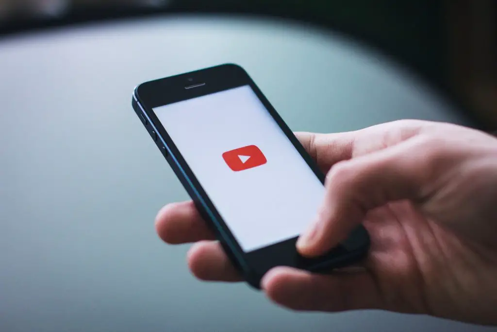 youtube channel or blogging hobby; male hand holding a smart phone with youtube logo on screen