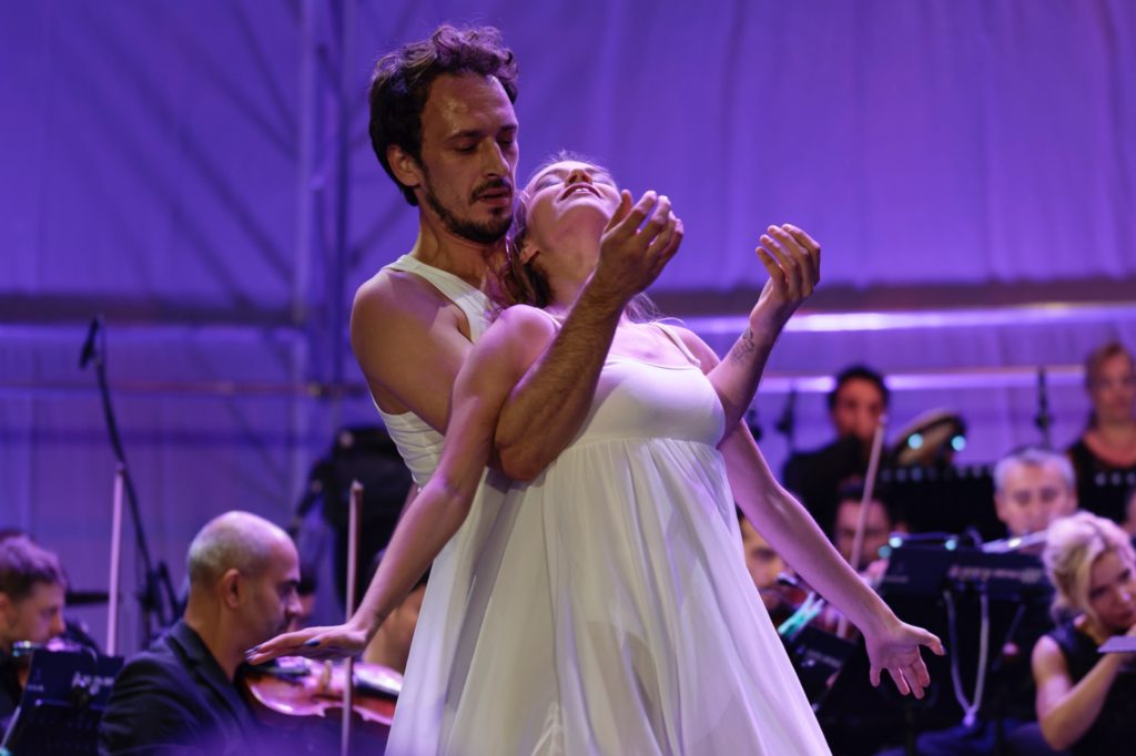 man and woman dancing in front of purple background and orchestra