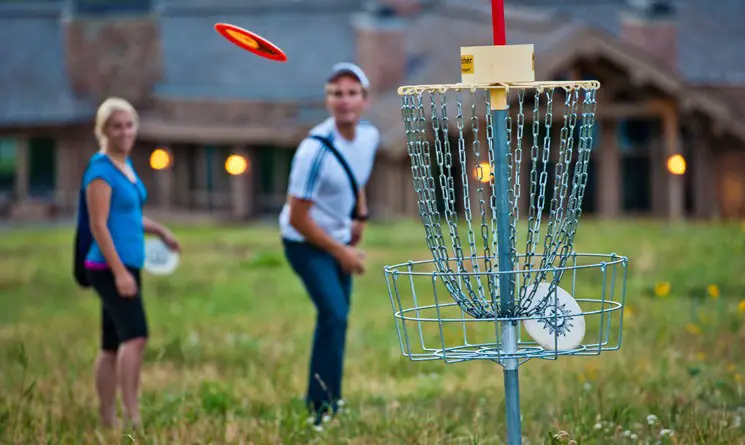 man and woman standing behind disc golf chain basket. Watching frisbee going towards basket
