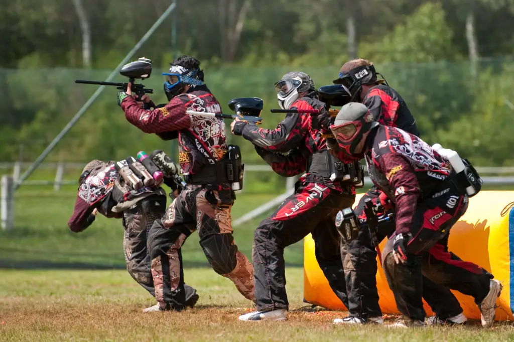 Five adult men, in full paintball gear shooting towards the opponents. Paintball hobbies for extroverts to get outdoors and get exercise