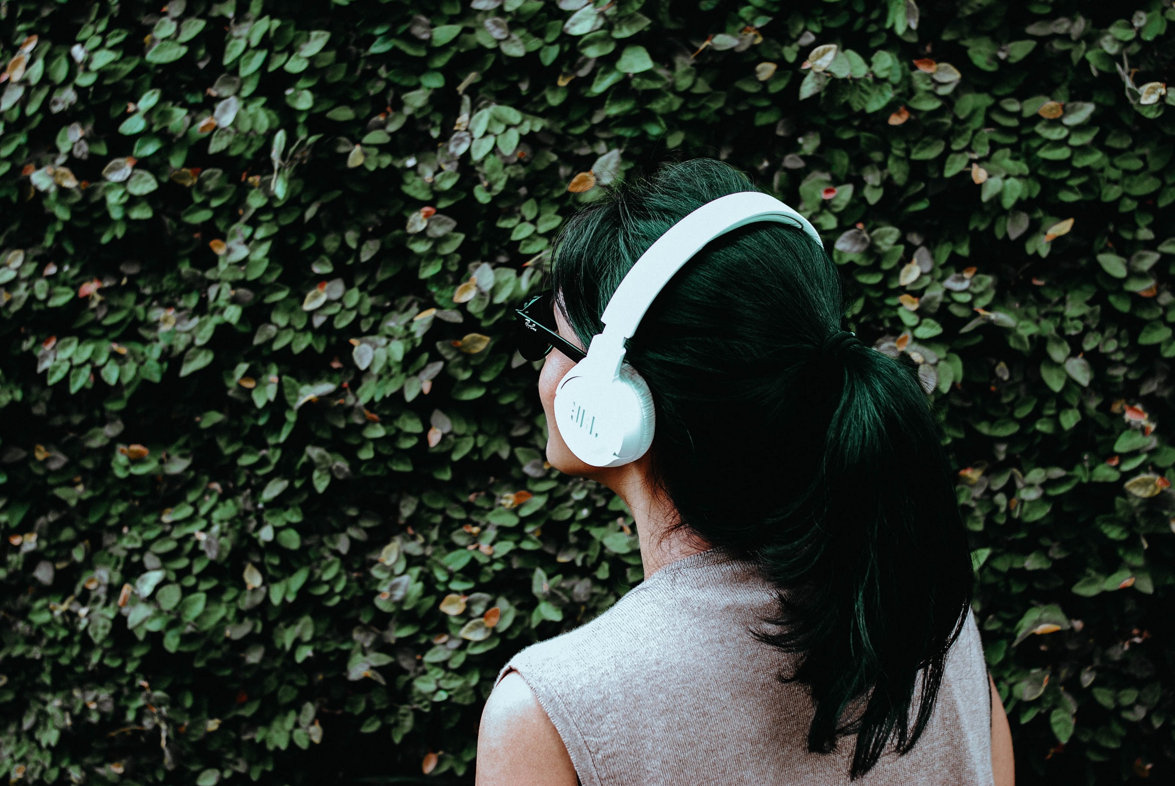 back view of woman looking at a green bush with headphones on