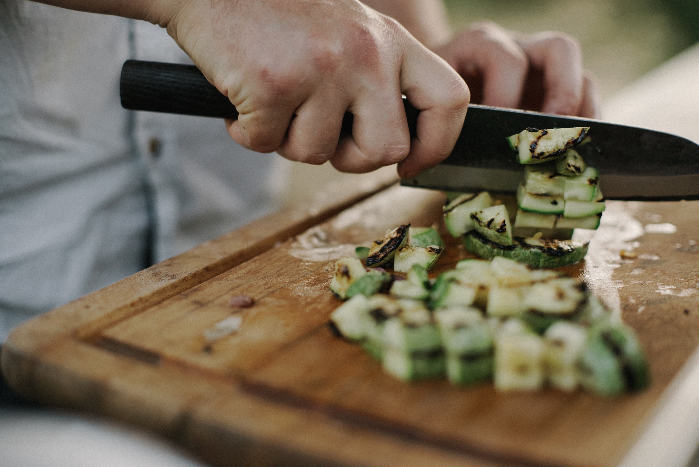 close up of hands chopping vegetables on a wooden cutting board