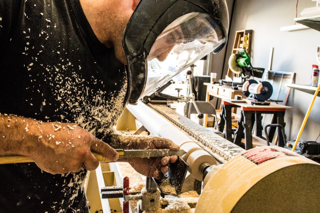 hobbies for stay-at-home dads include woodworking.  Man carving wood in garage with face covering protection