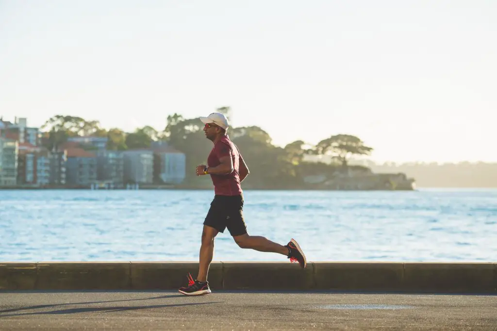 hobbies for weight loss include running. Pictures is a man running near waterfront at sunrise