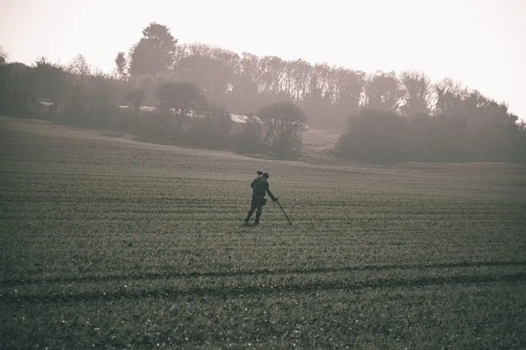 Man is a field with a metal detector walking for weight loss and leisure 
