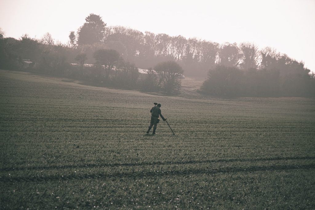 Man is a field with a metal detector walking for weight loss and leisure 