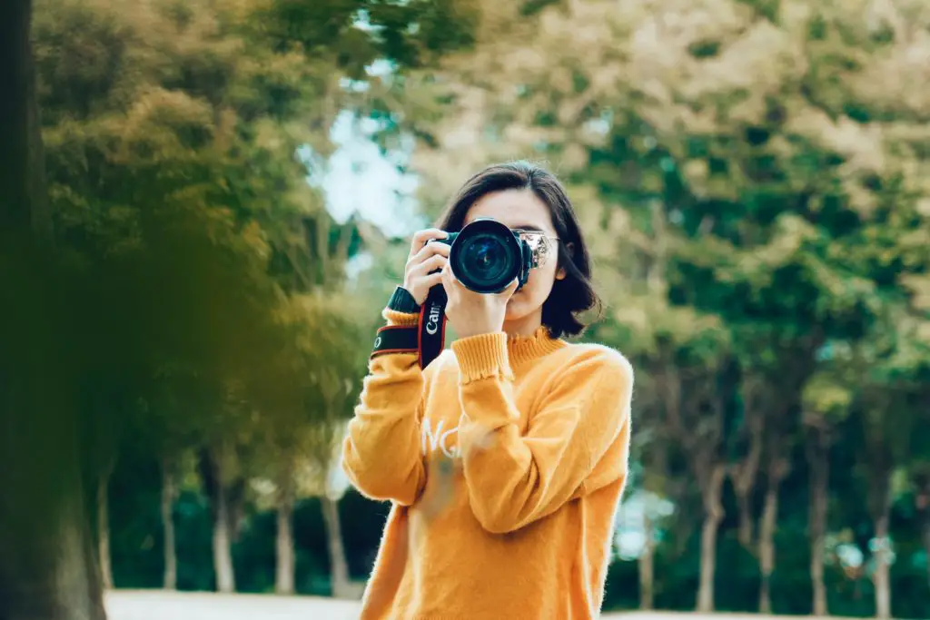 photography hobby for stay-at-home moms woman in yellow sweater aiming camera towards viewer