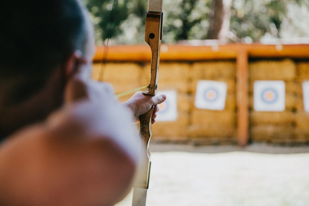 hobbies for stay-at-home dads include archery.  View from mans elbow, pulling back arrow aimed at distant blurred target