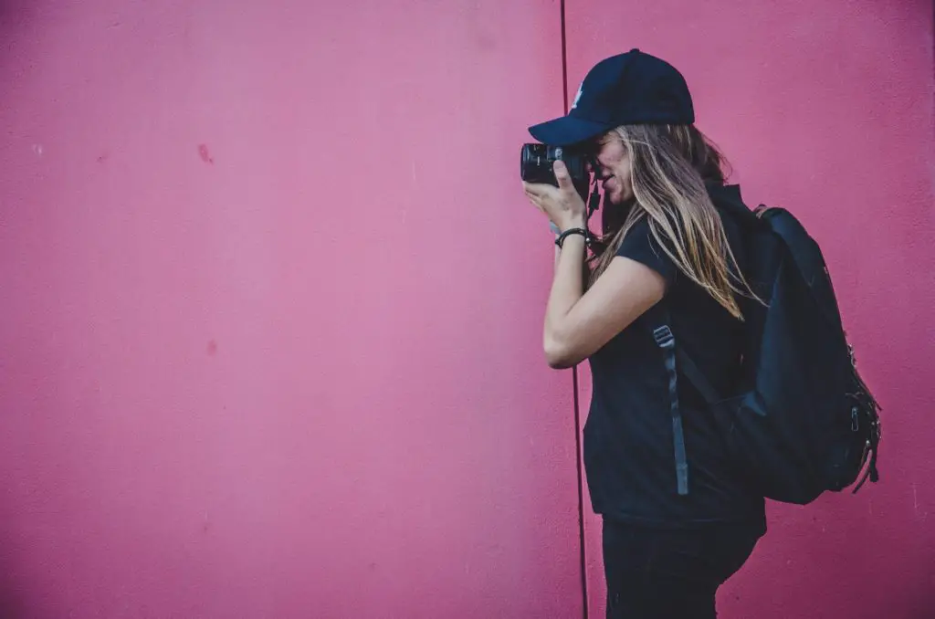 side profile of a woman with camera to her eye in front of pink wall