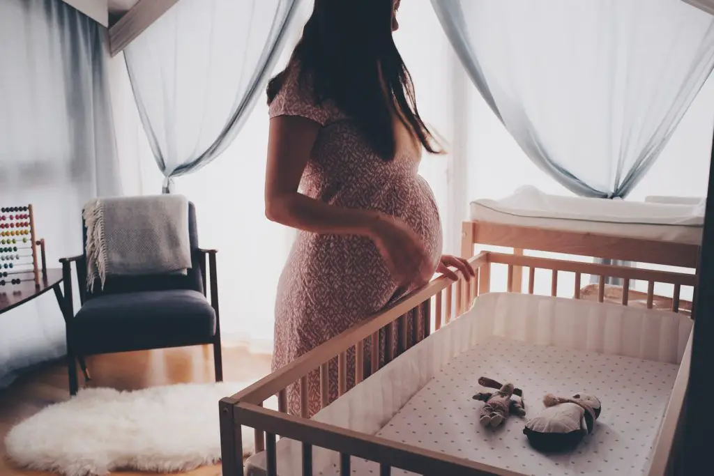 pregnant woman looking at empty cradle awaiting baby.  Nesting and interior design is a great hobby for pregnant women to prepare for their coming child.