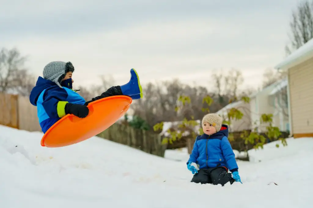 outdoor winter hobby sledding two children one airborne on sled