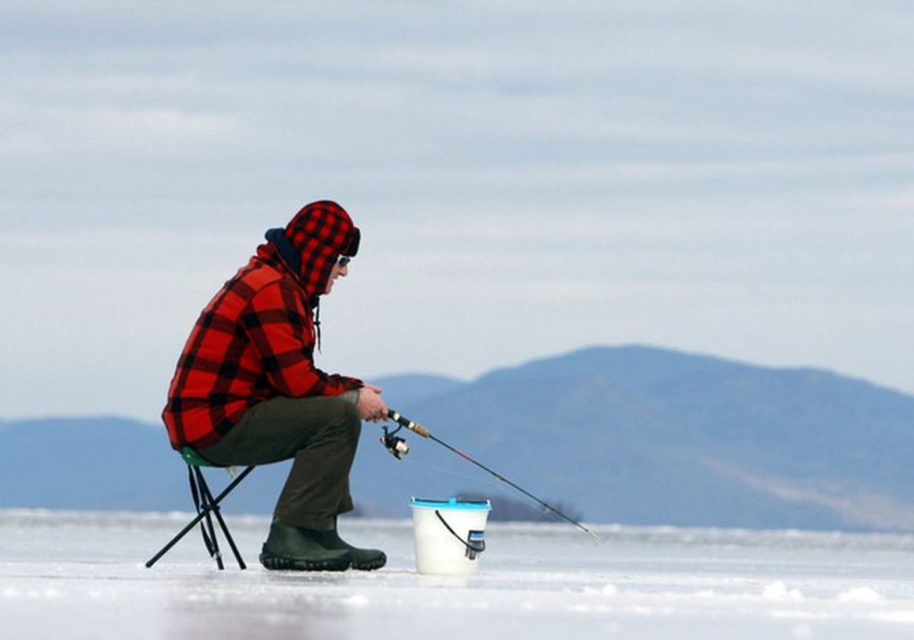 outdoor winter hobby ice fishing; man sitting over ice fishing hole 