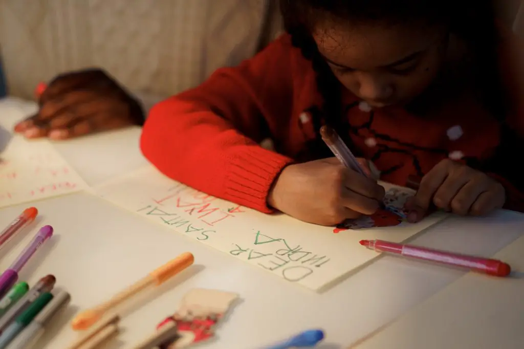 young girl writing a letter to santa with multi color pens