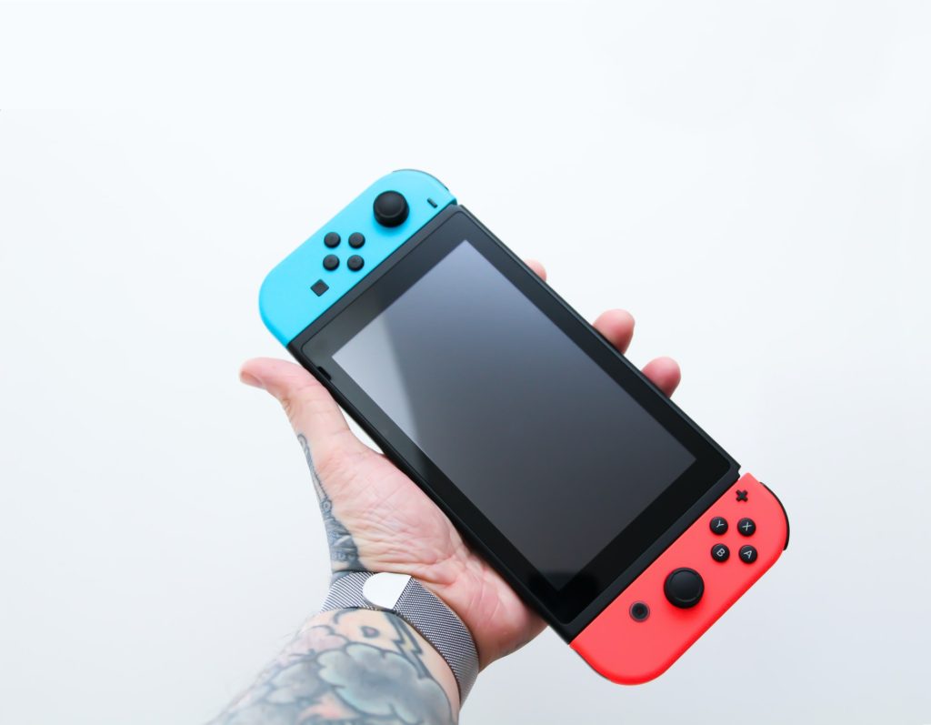 man with tattooed arm holding a handheld video game device