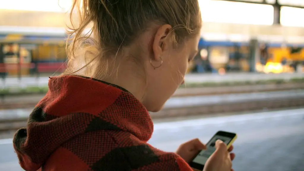 over-shoulder view of woman looking at cellphone waiting for train