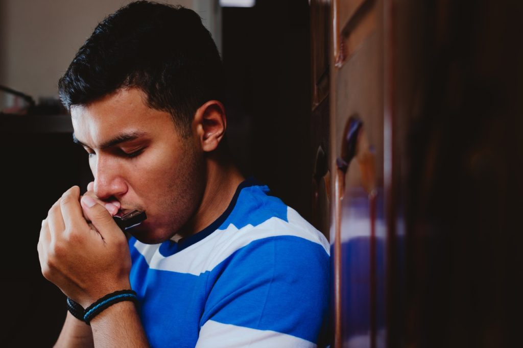 man playing harmonica with eyes closed indoors