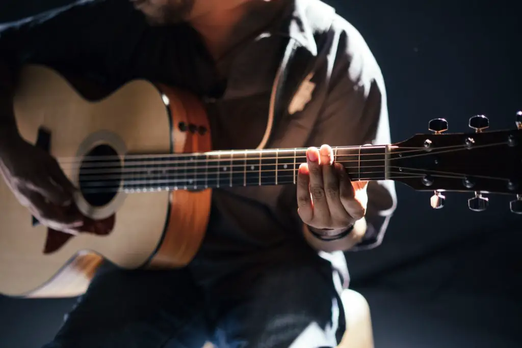 list of hobbies includes playing guitar.  Close of backlit view of mans hands playing acoustic guitar