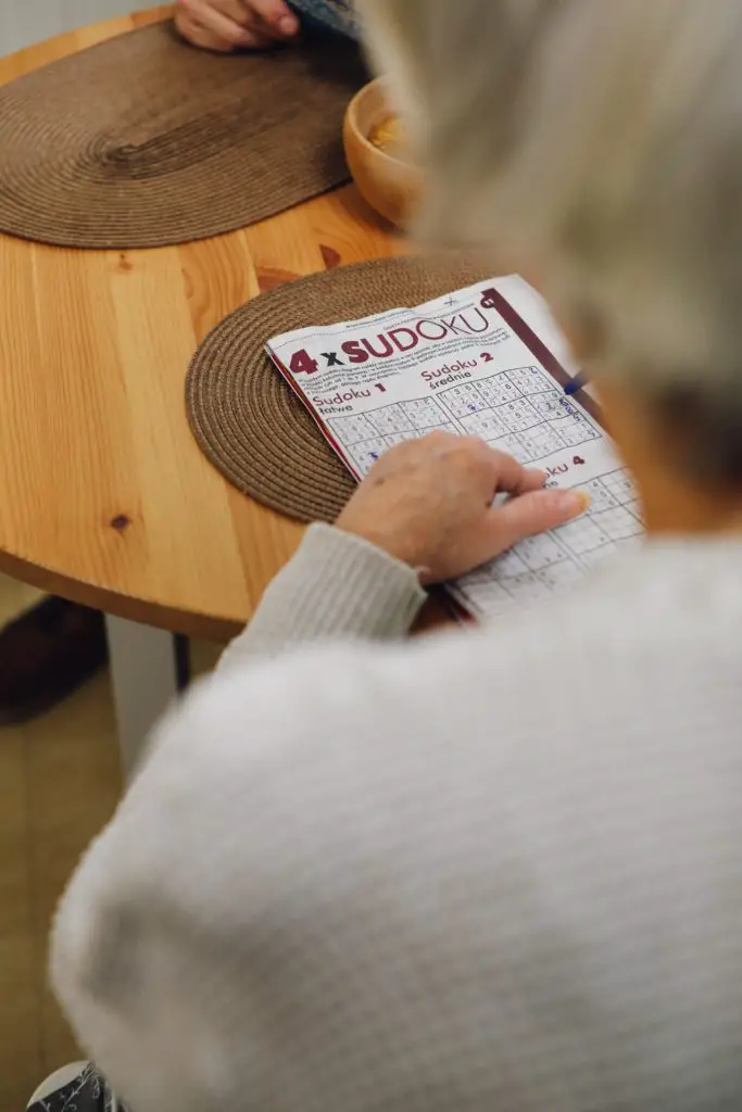 overhead view of older woman doing free hobby sudoku puzzle