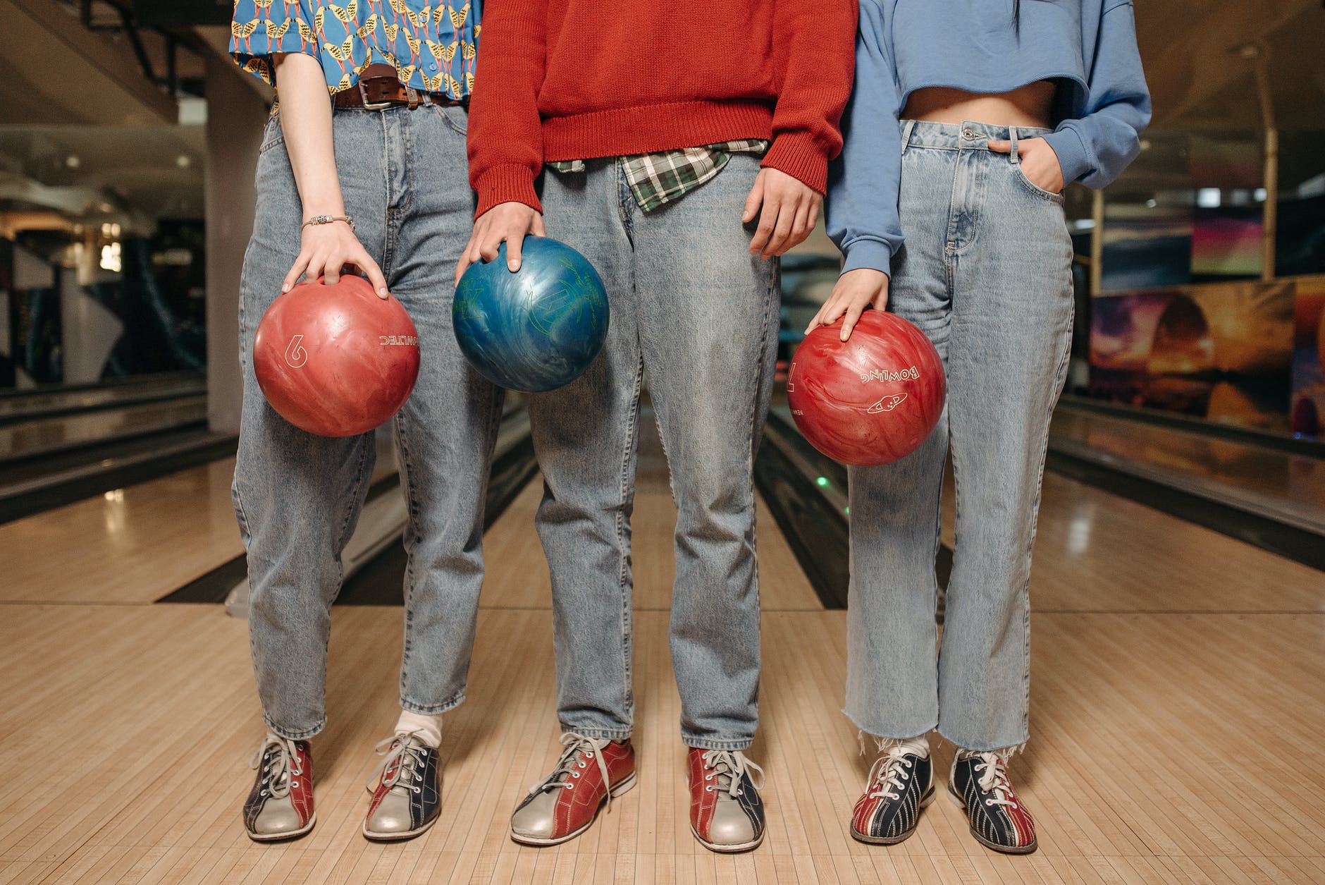 people in gray denim jeans holding bowling balls standing side by side