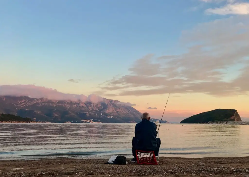 fishing quotes image, old man sitting on shore with fishing rod looking at sunrise sky