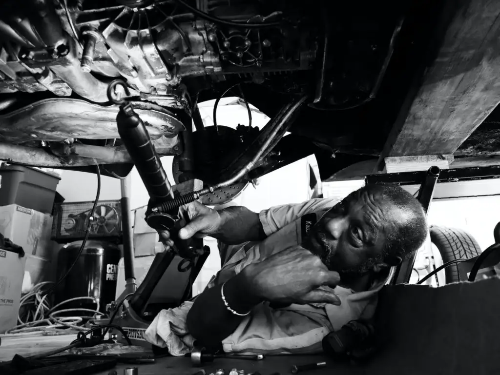 retirement activities auto maintenance black and white man working under car