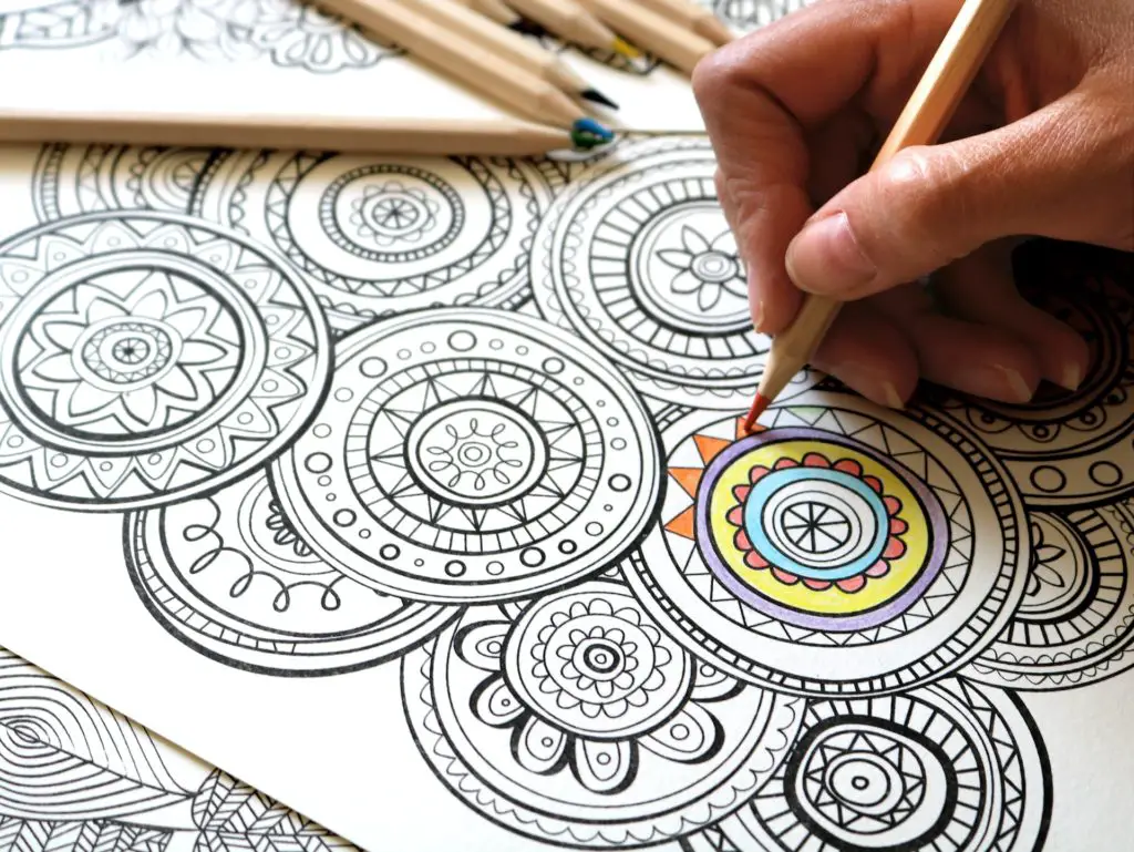 close up of hands coloring small mandalas with colored pencils