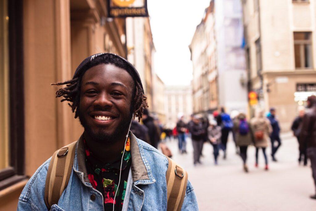 man smiling with headphones in on crowded street.  Listening to music hobby to make money