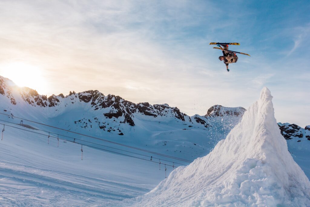 man upside down after riding up ski jump, mountain and setting sun in background