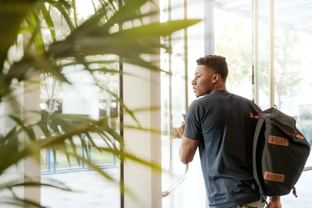 young black man leaving school building with backpack, looking hopeful