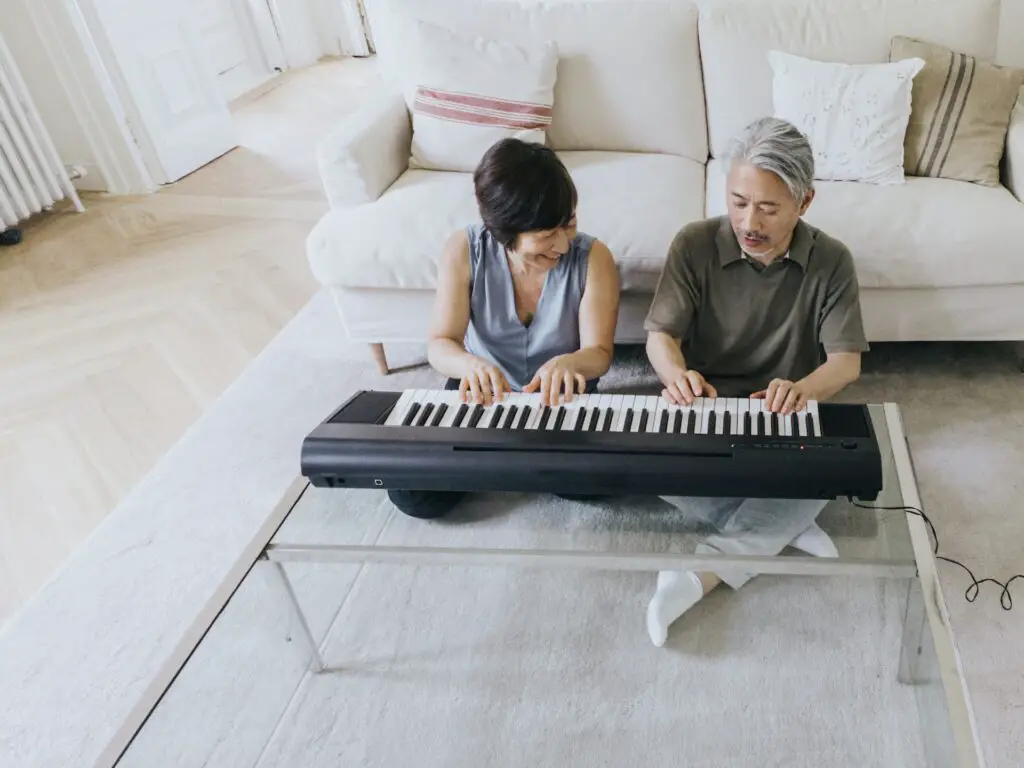 asian husband and wife playing keyboard sitting on the floor leaning against a couch